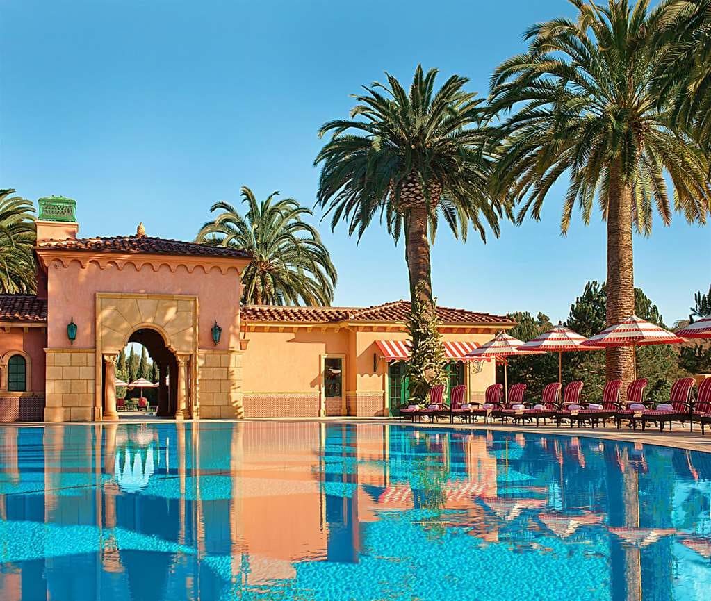 A palm-lined pool reflecting the resort's Mediterranean arches