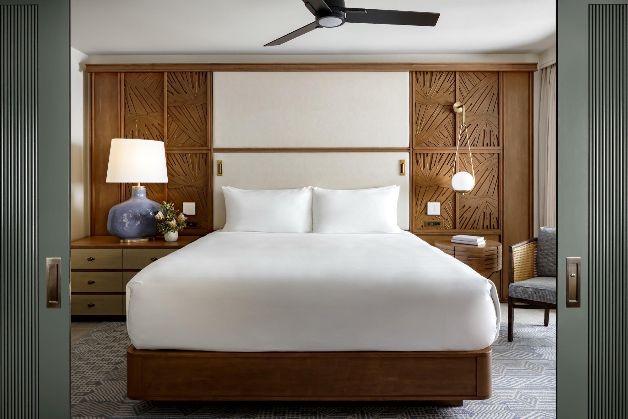 A Kilohana suite bedroom with a king bed between carved wood panels