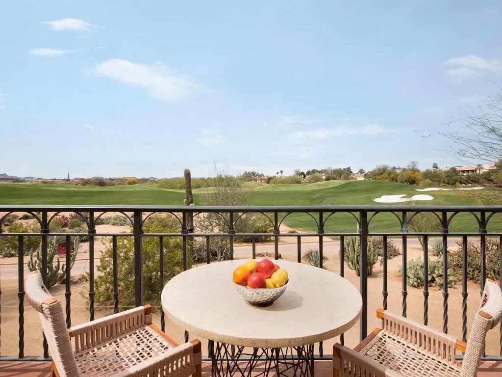 A balcony table with a bowl of fruit, looking over desert and a golf course