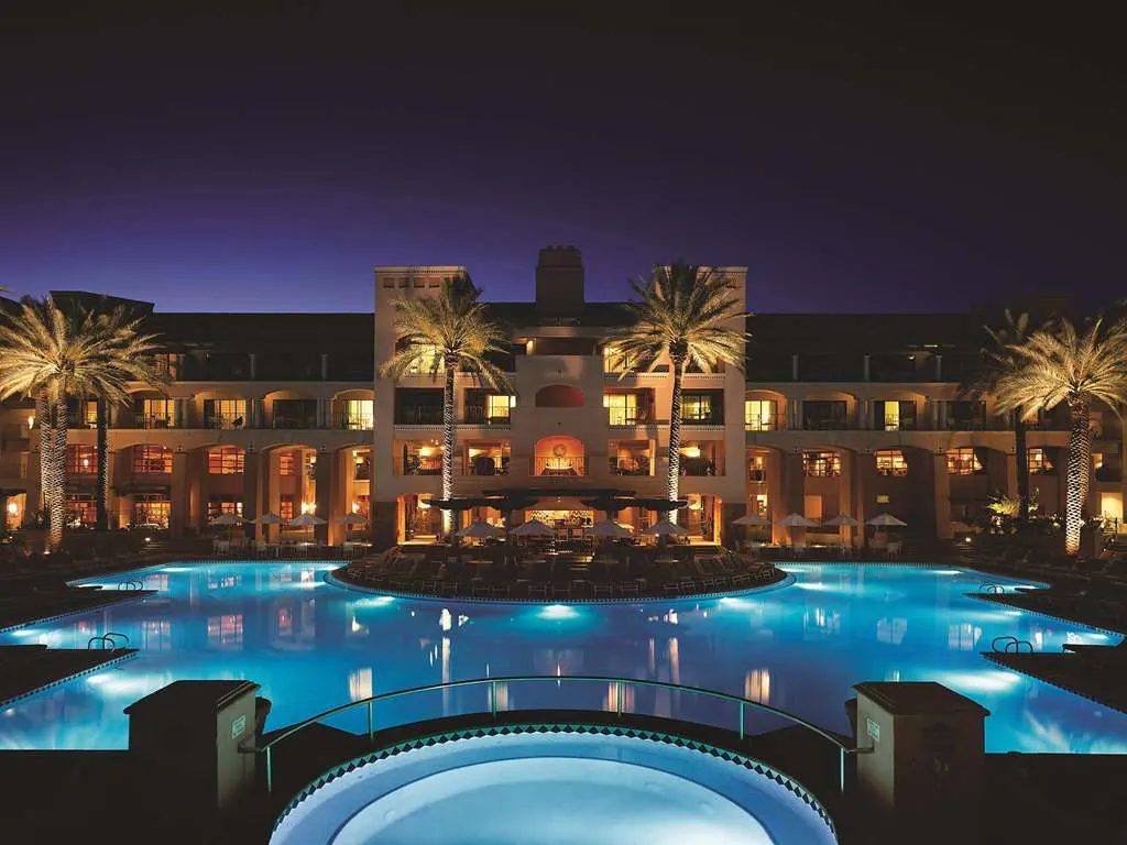 The main pool glowing blue at night before the lit resort and its palms