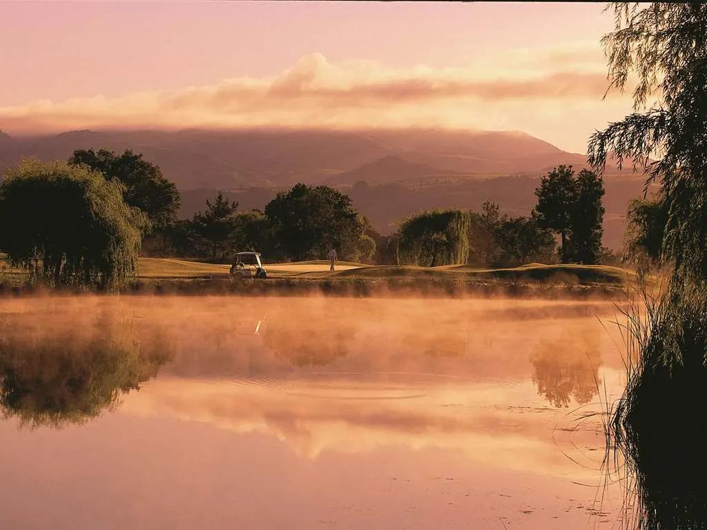 Morning mist rising off a still pond, with the valley hills glowing beyond