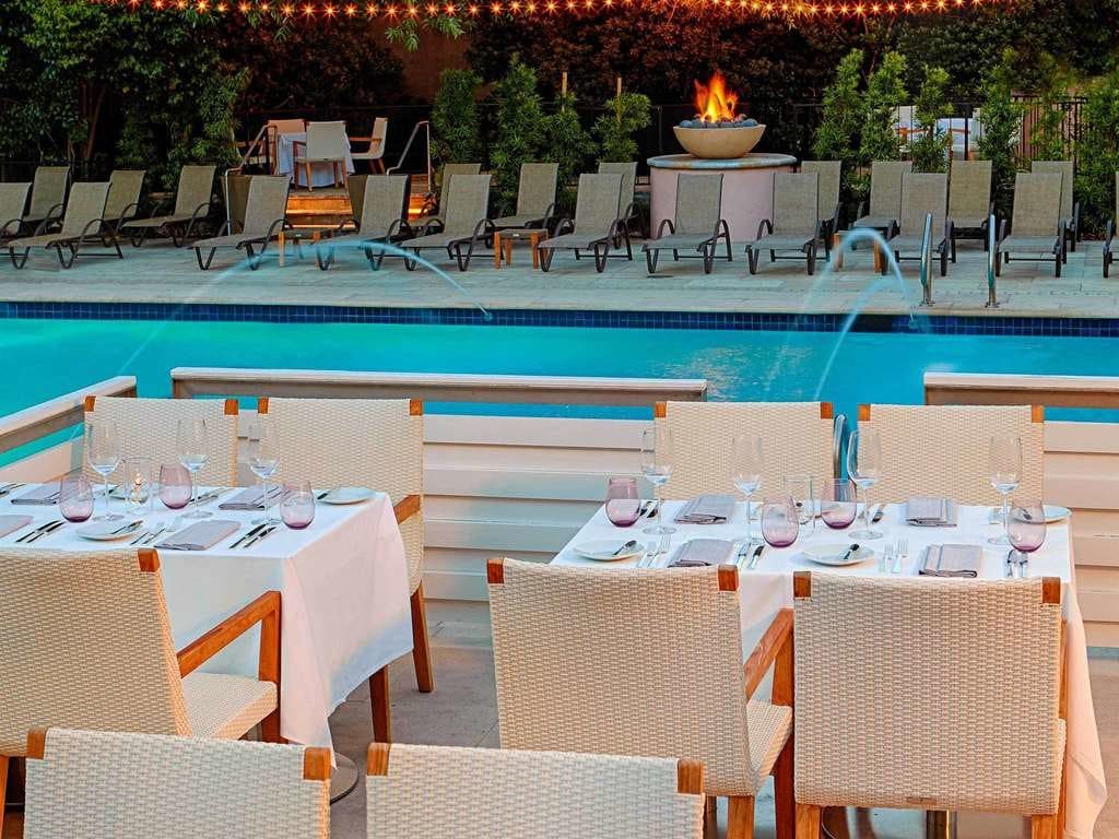 Tables set for dinner beside the pool, with a fire bowl and loungers behind