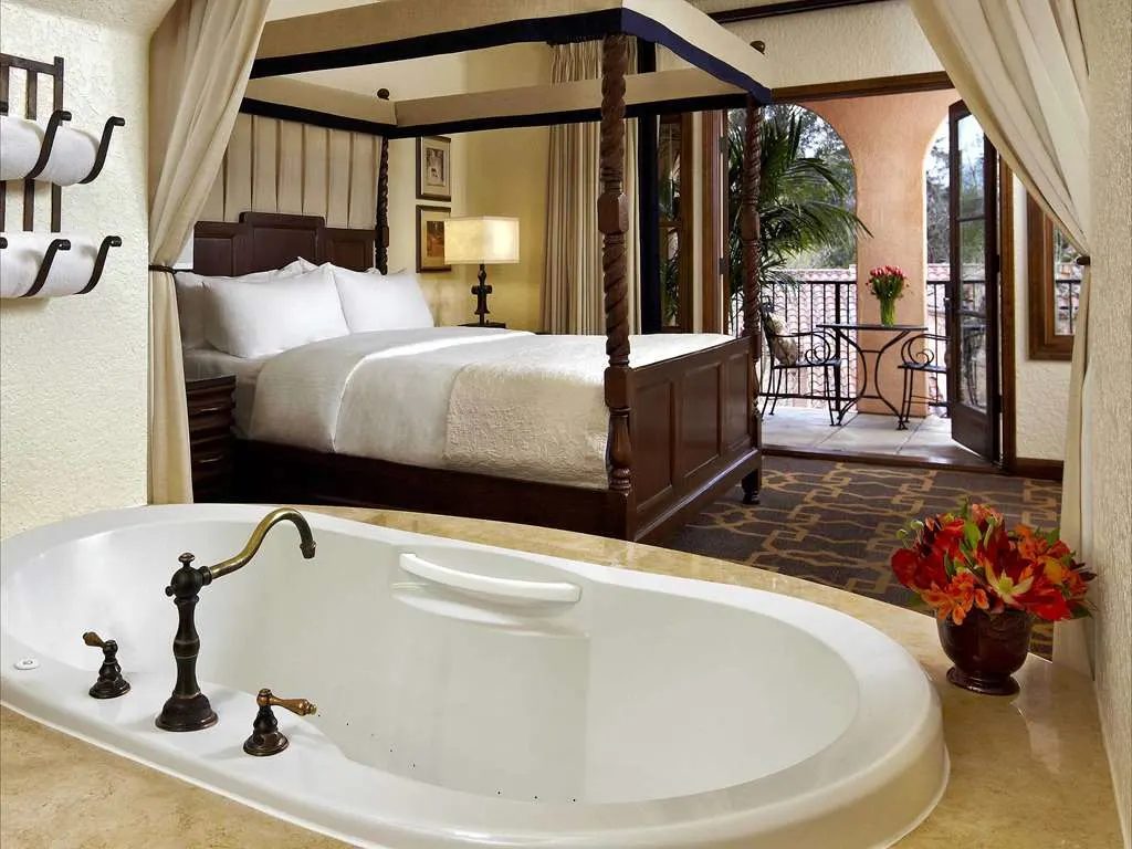 A suite with a four-poster bed, a soaking tub, and a balcony