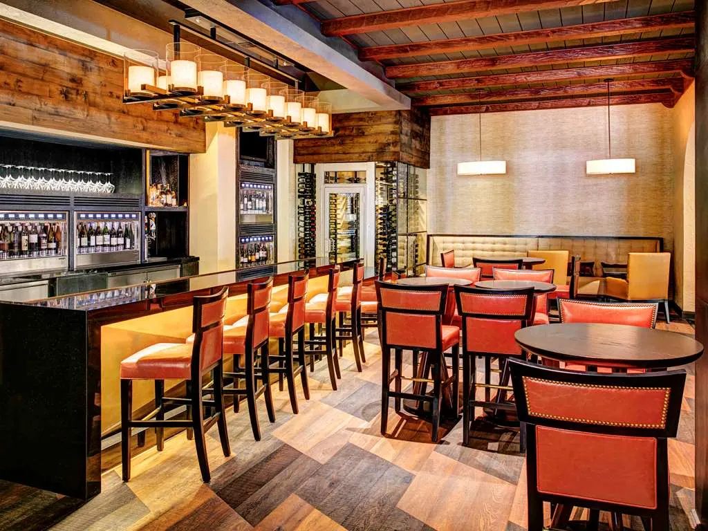 A wine bar with tall orange chairs and wine dispensers under wood beams