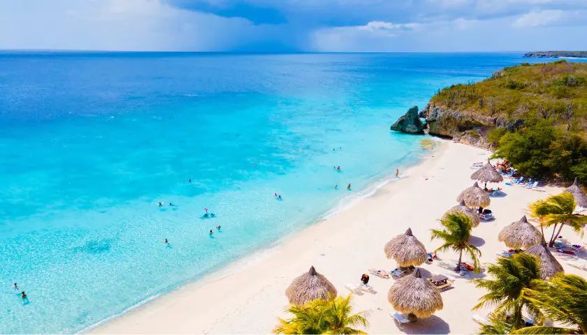 A white-sand Caribbean beach with palm-thatched umbrellas and turquoise water