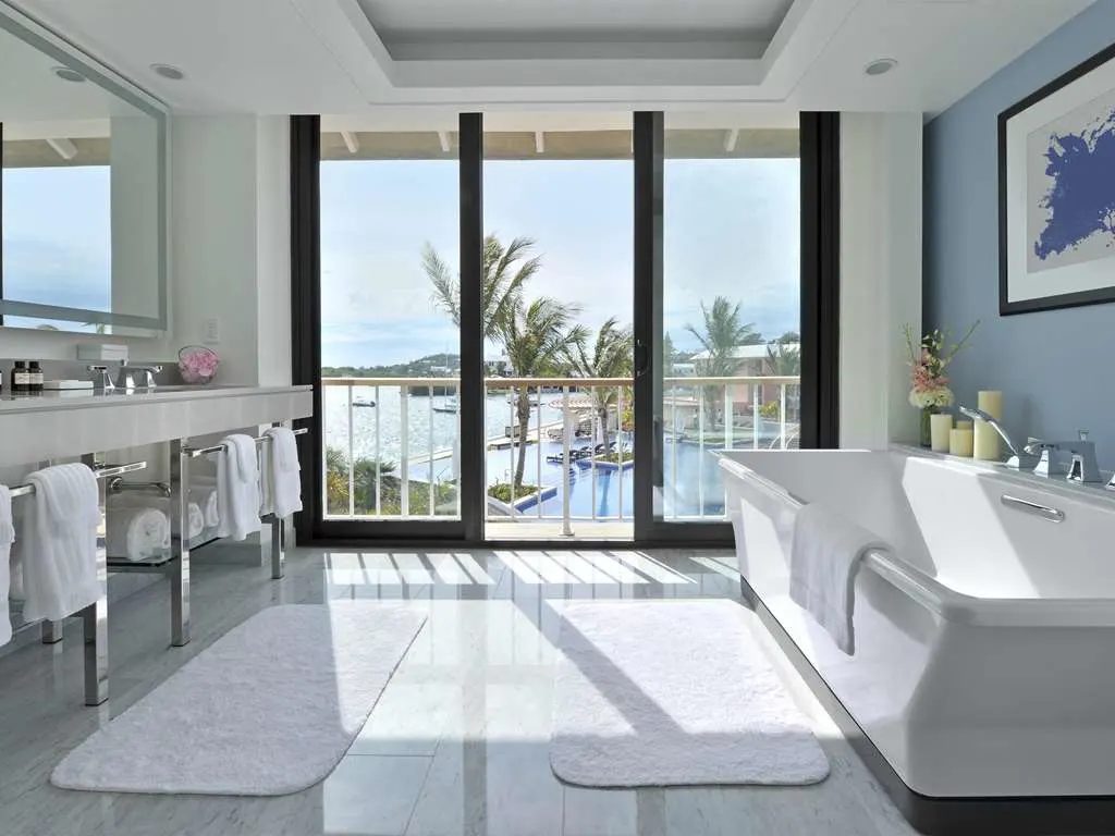 A marble bathroom with a freestanding tub and glass doors to a harbor view