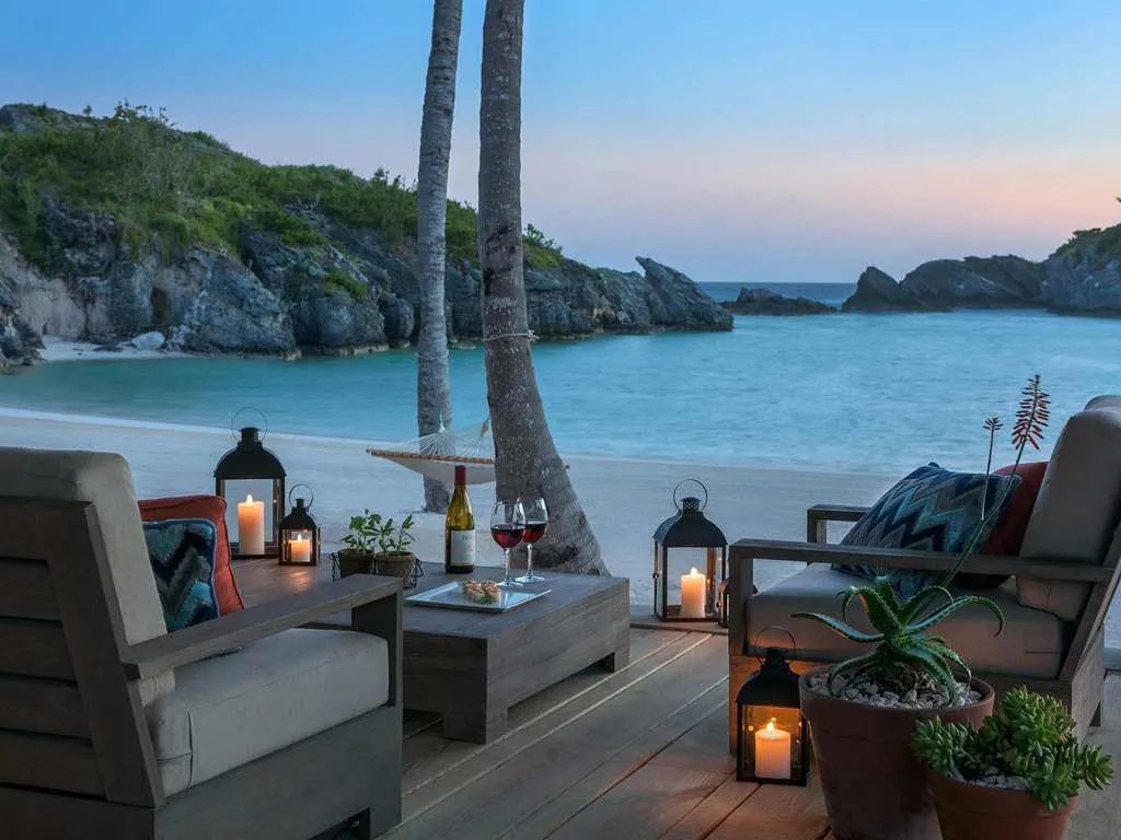 Lanterns and armchairs on a deck above a quiet cove at dusk