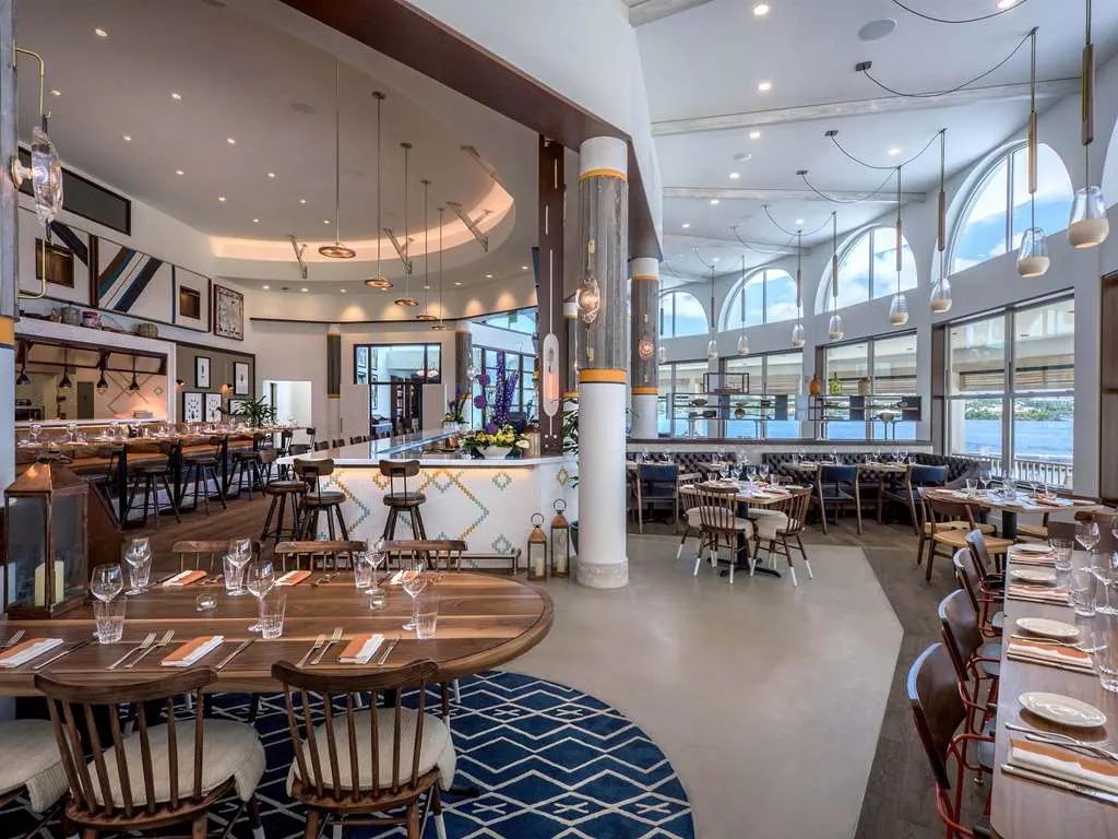 A bright restaurant with arched windows, an open kitchen, and a blue patterned rug