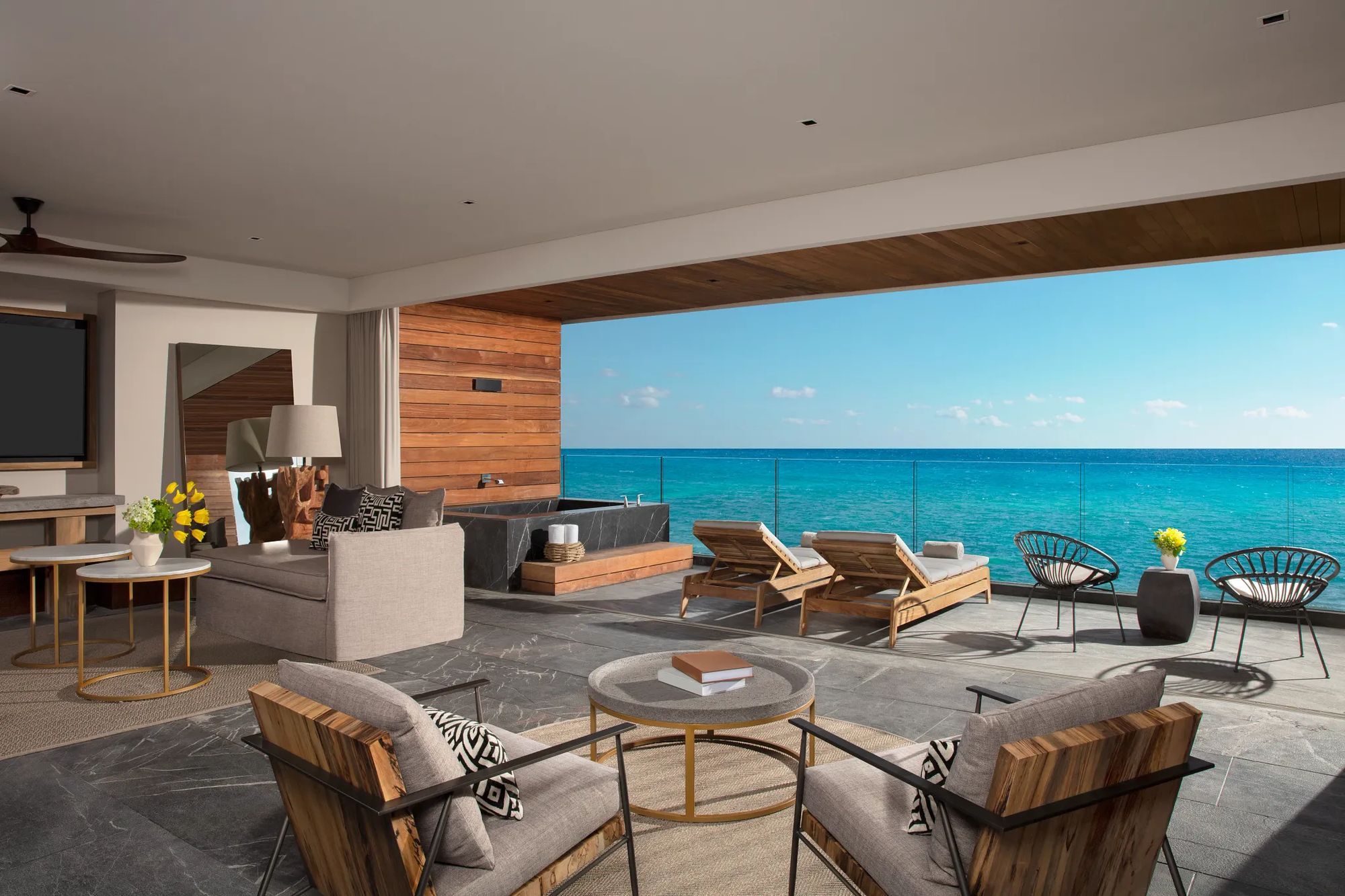 An oceanfront suite with a bed, sitting area, and wall of glass