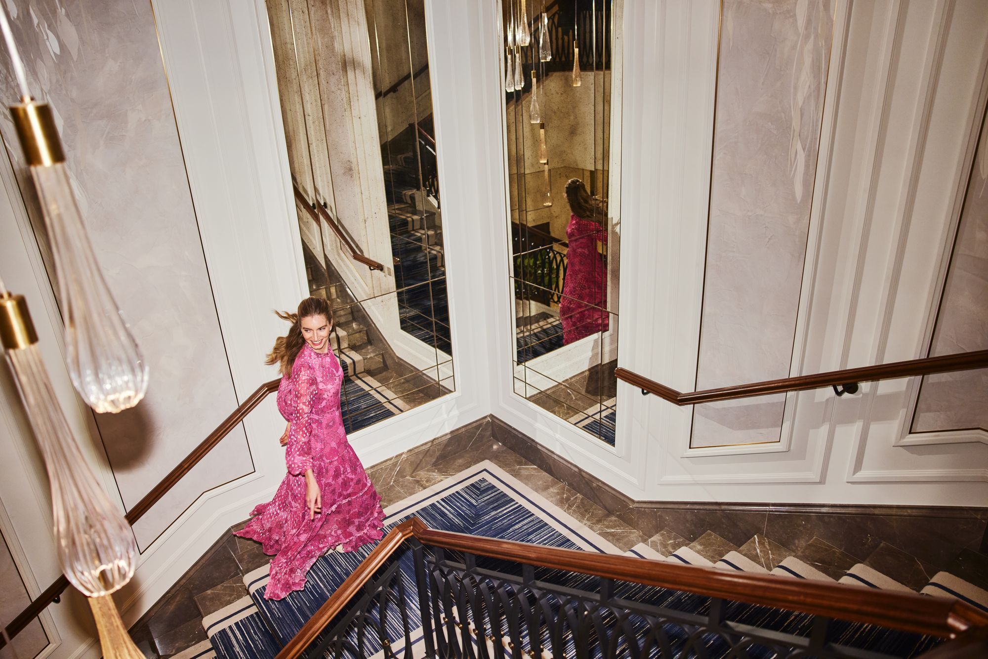 A guest in a pink dress descending the hotel's grand staircase