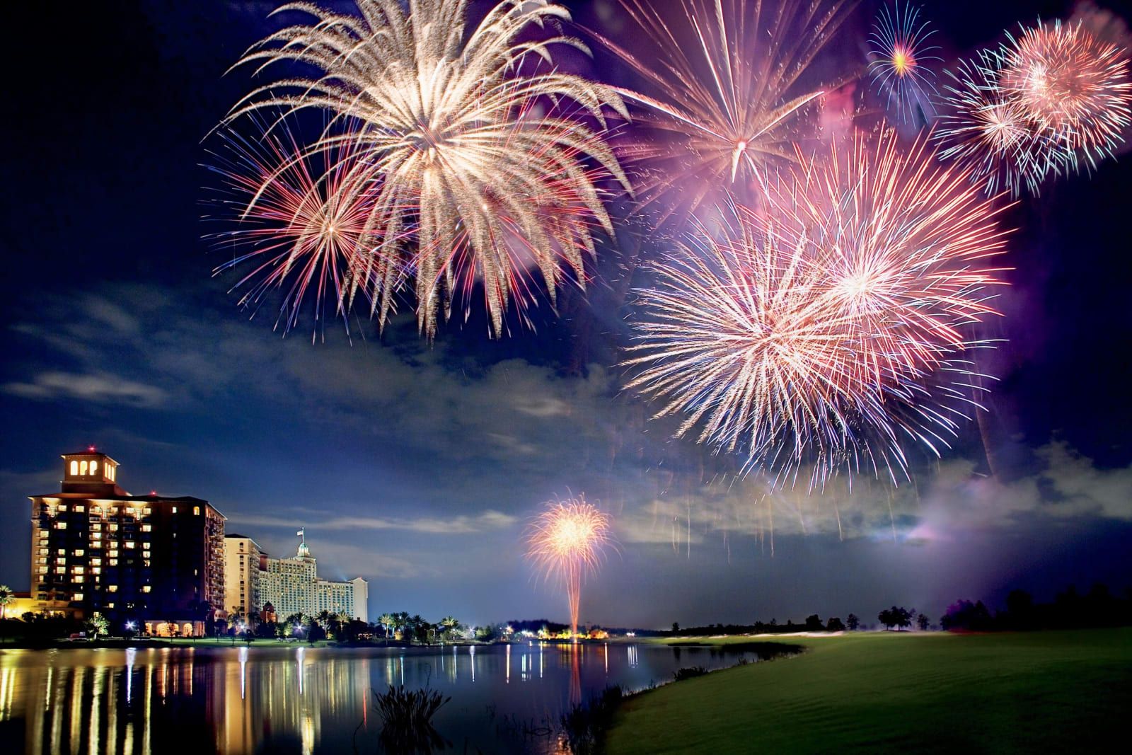 Fireworks bursting over the lake beside the lit resort tower