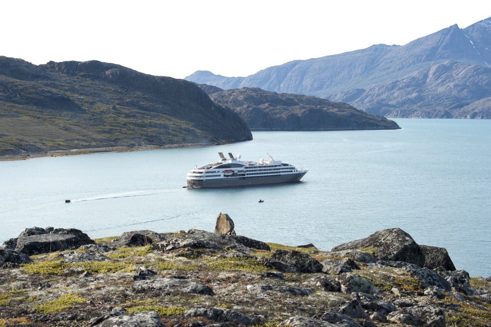 A small PONANT expedition ship in a quiet fjord beneath rocky hills