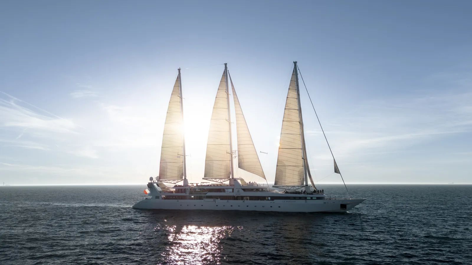 A three-masted sailing yacht under full sail at golden hour
