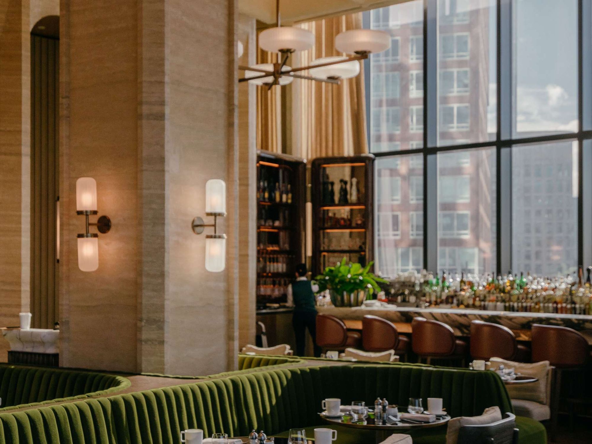 A bar with green banquettes beneath brass lights