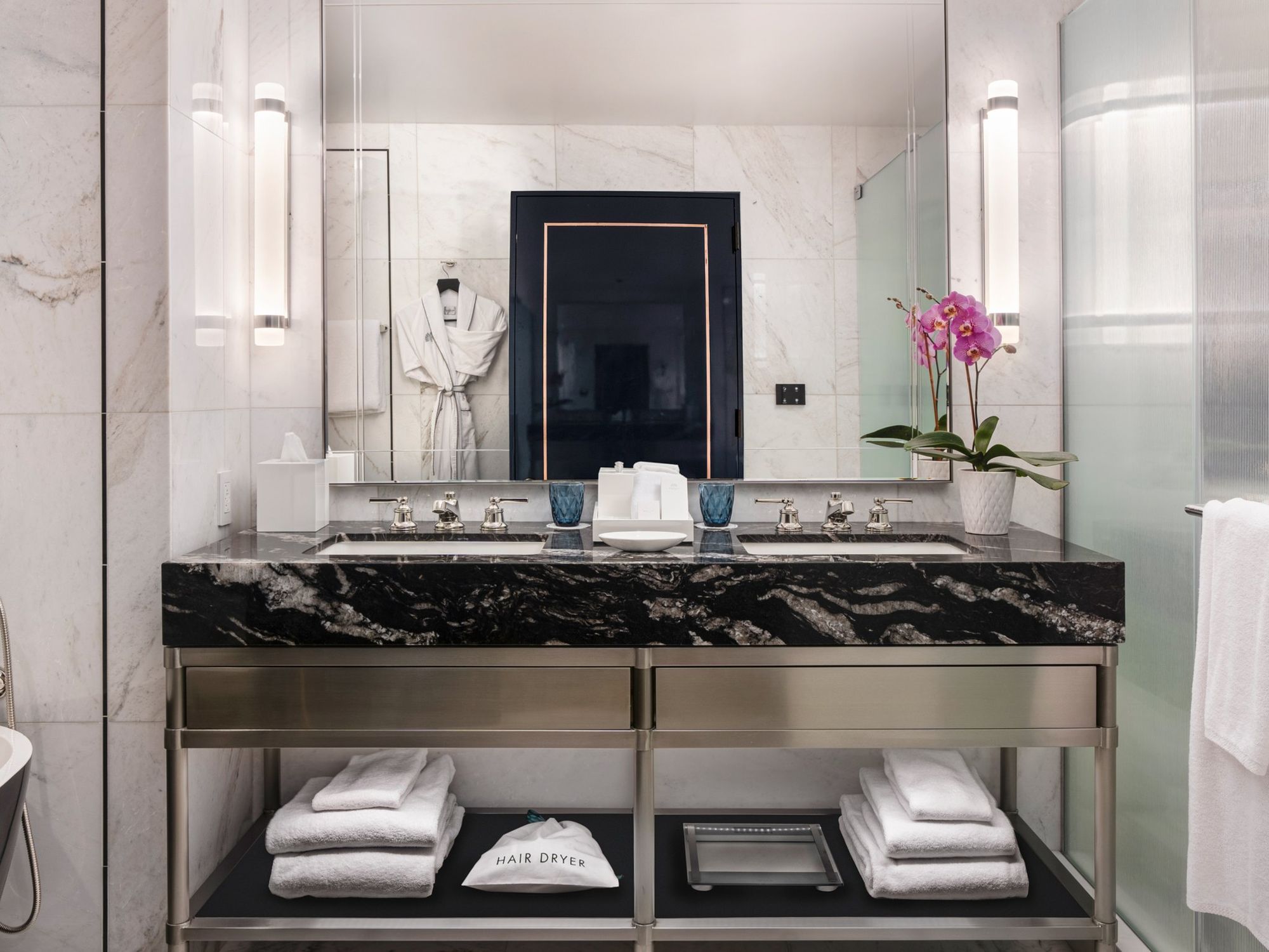 A marble bathroom with a double vanity and an orchid