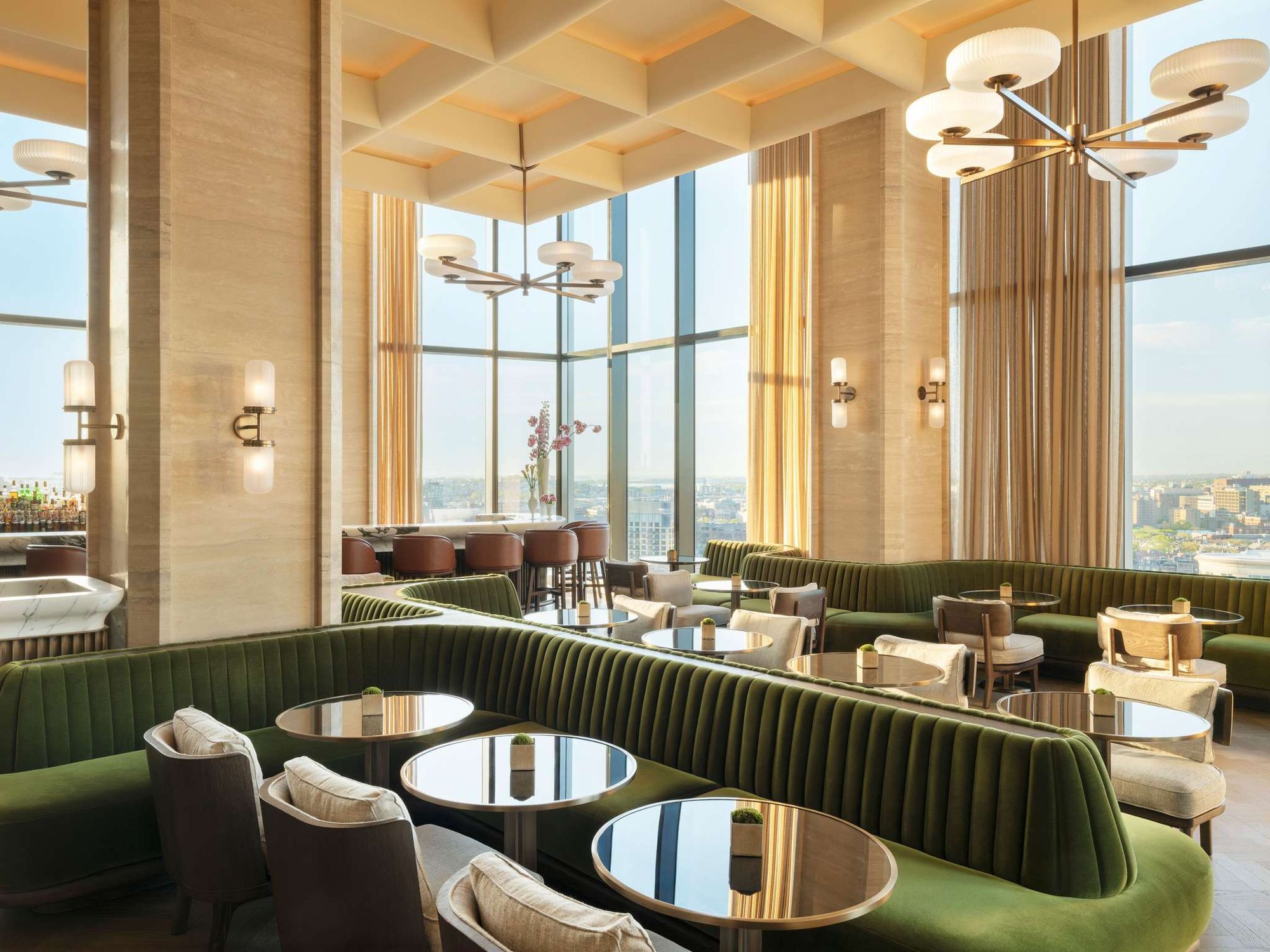 The sky lounge at Raffles Boston, a Fora Reserve hotel, with green velvet banquettes and tall windows