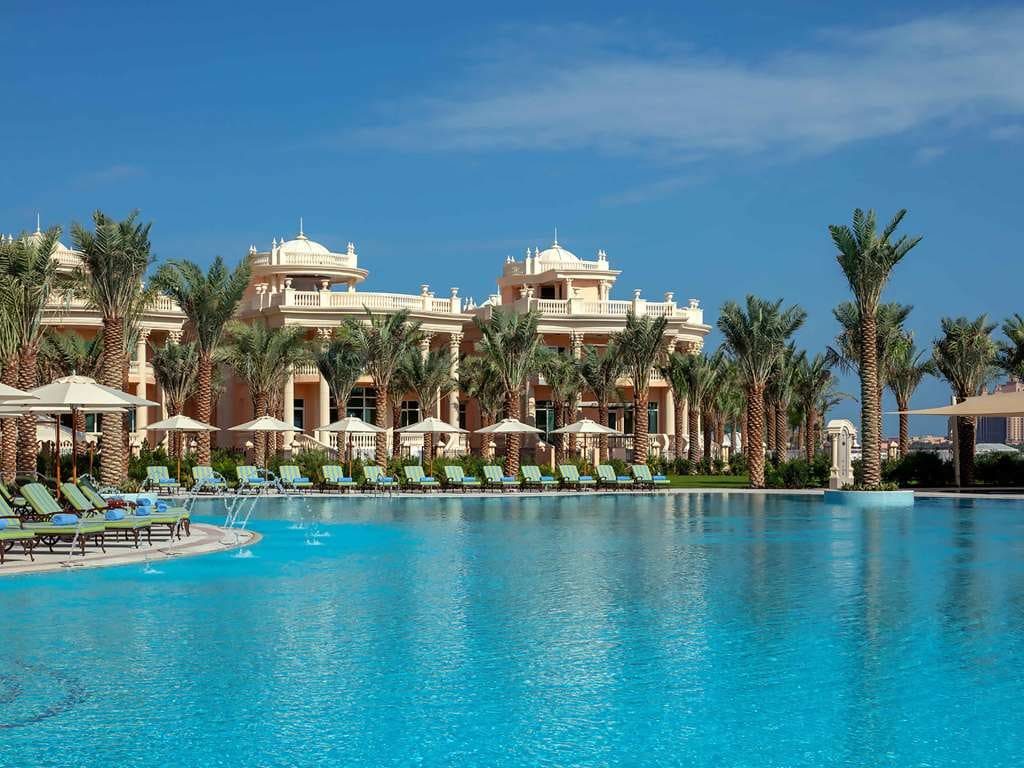 A long blue pool lined with palms and loungers before the palace-style resort
