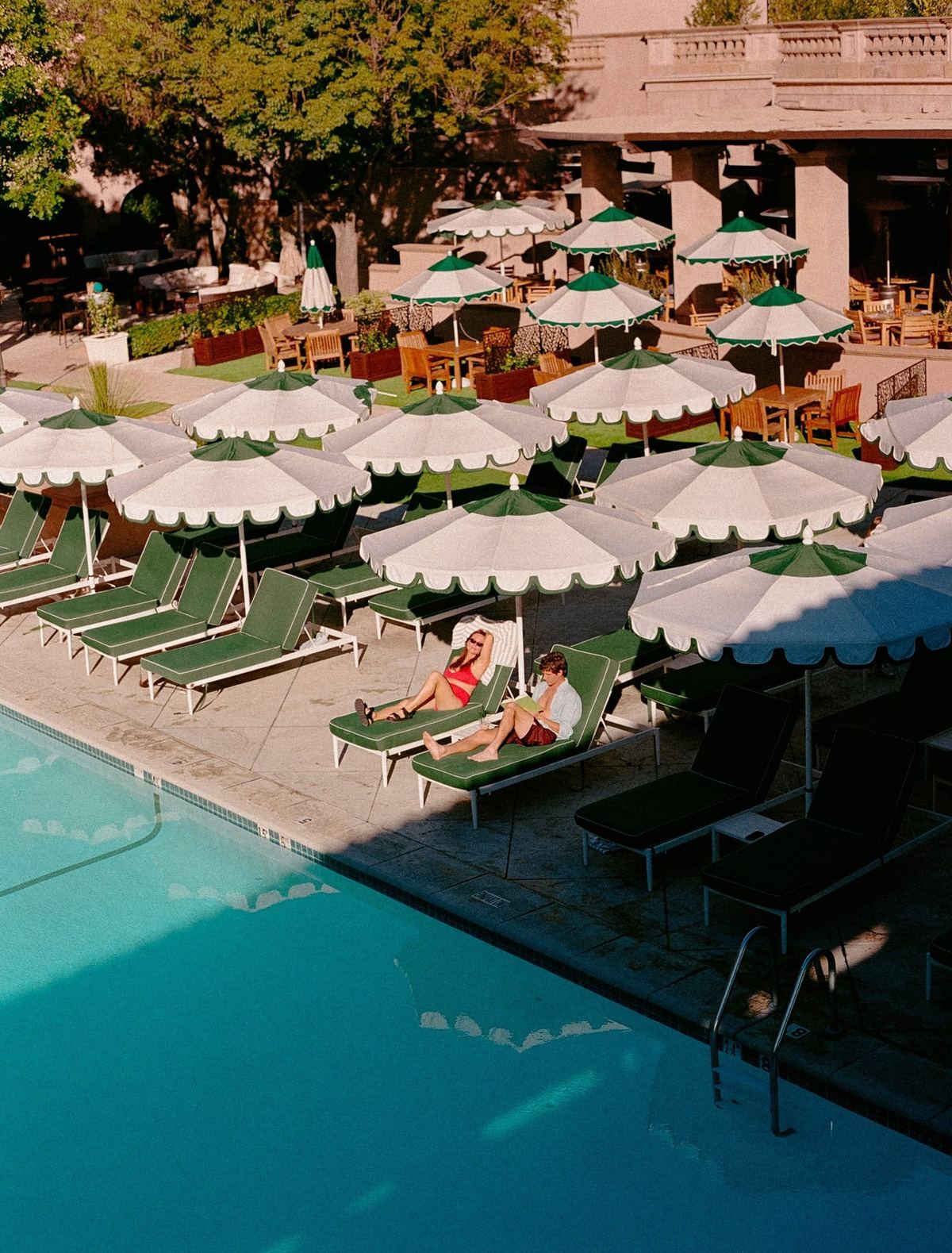 Rows of white umbrellas and green loungers beside a hotel pool