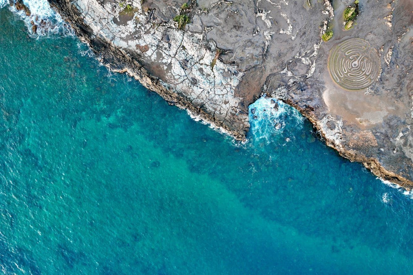 Aerial view of clear blue water against the lava-rock shore