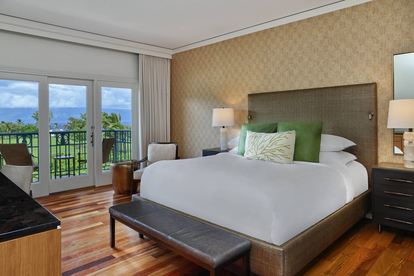 A guest room with a green-accented bed and doors open to a balcony