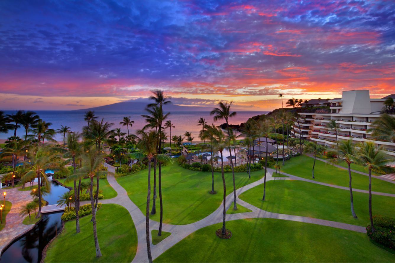 The resort lawns and palms under a vivid sunset, with Lanai on the horizon