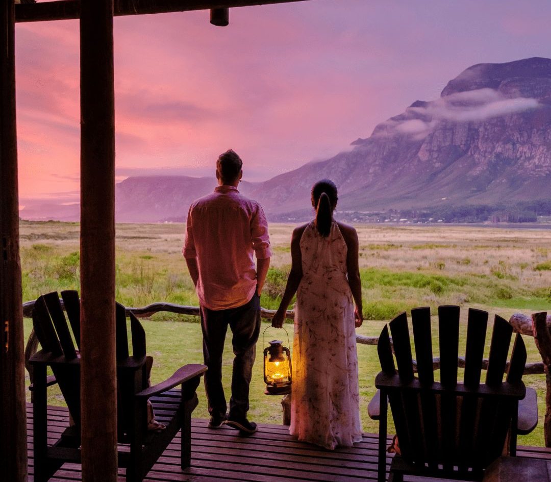 A couple on a safari lodge porch at dusk, looking out to the mountains