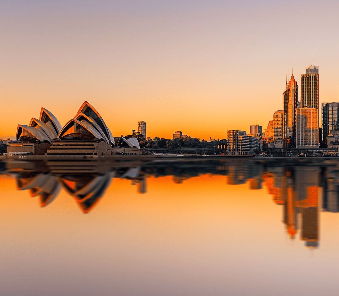 The Sydney Opera House and skyline reflected in the harbor at sunset